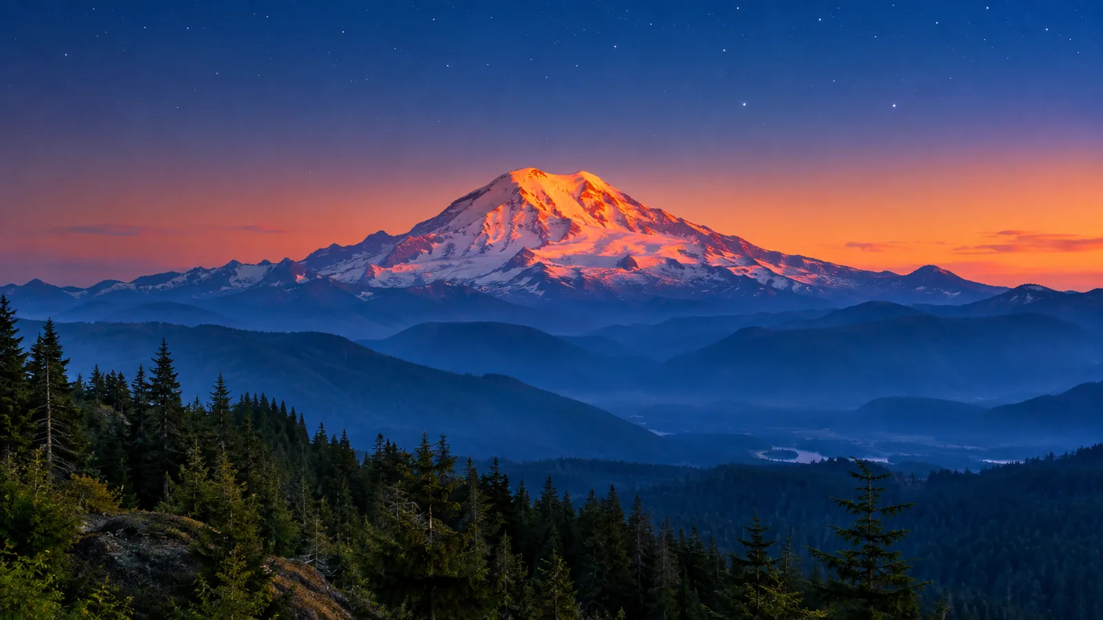 Mount Rainier glowing with alpenglow above forested ridges at dusk